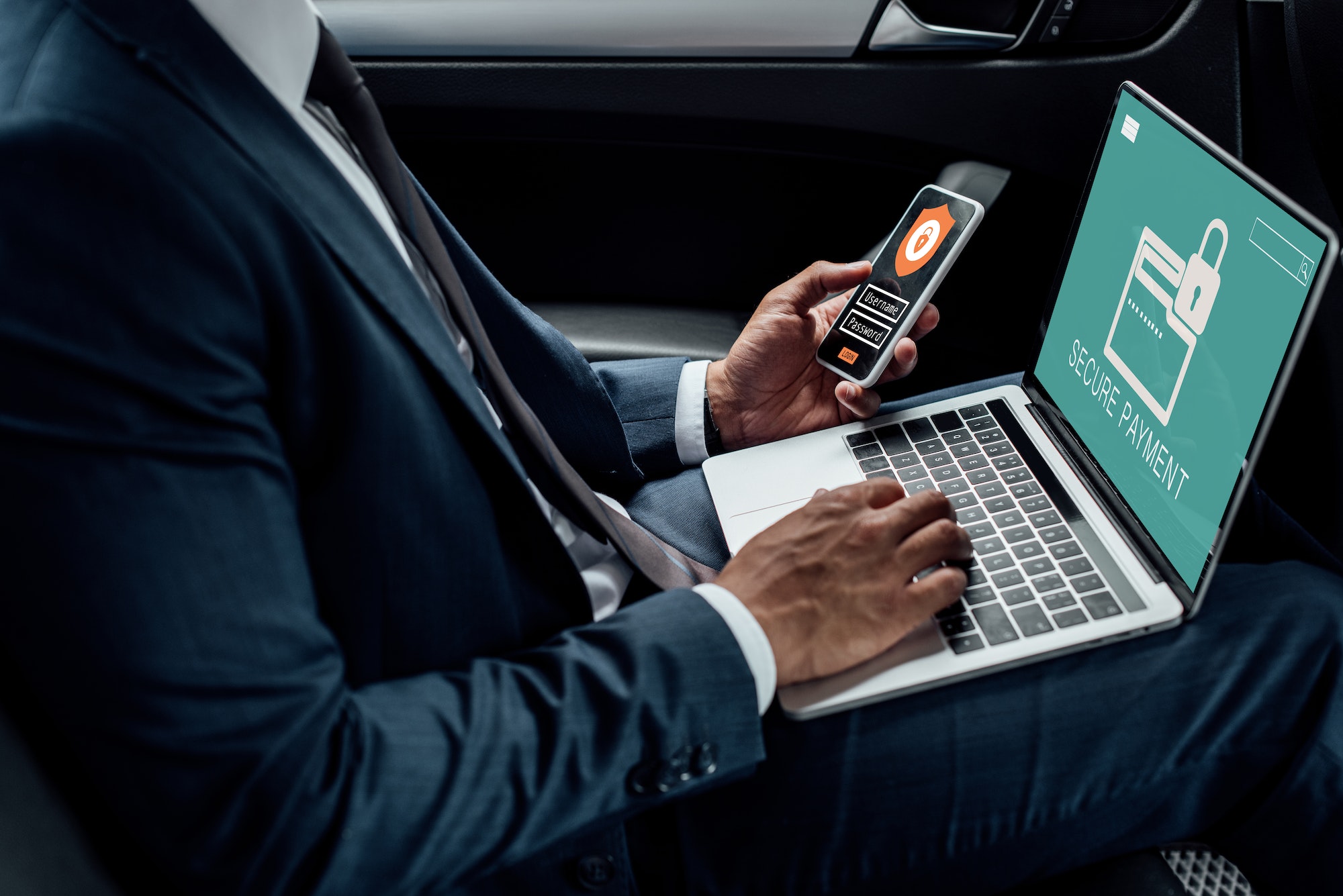 Cropped view of african american businessman using laptop and smartphone in car with cyber security